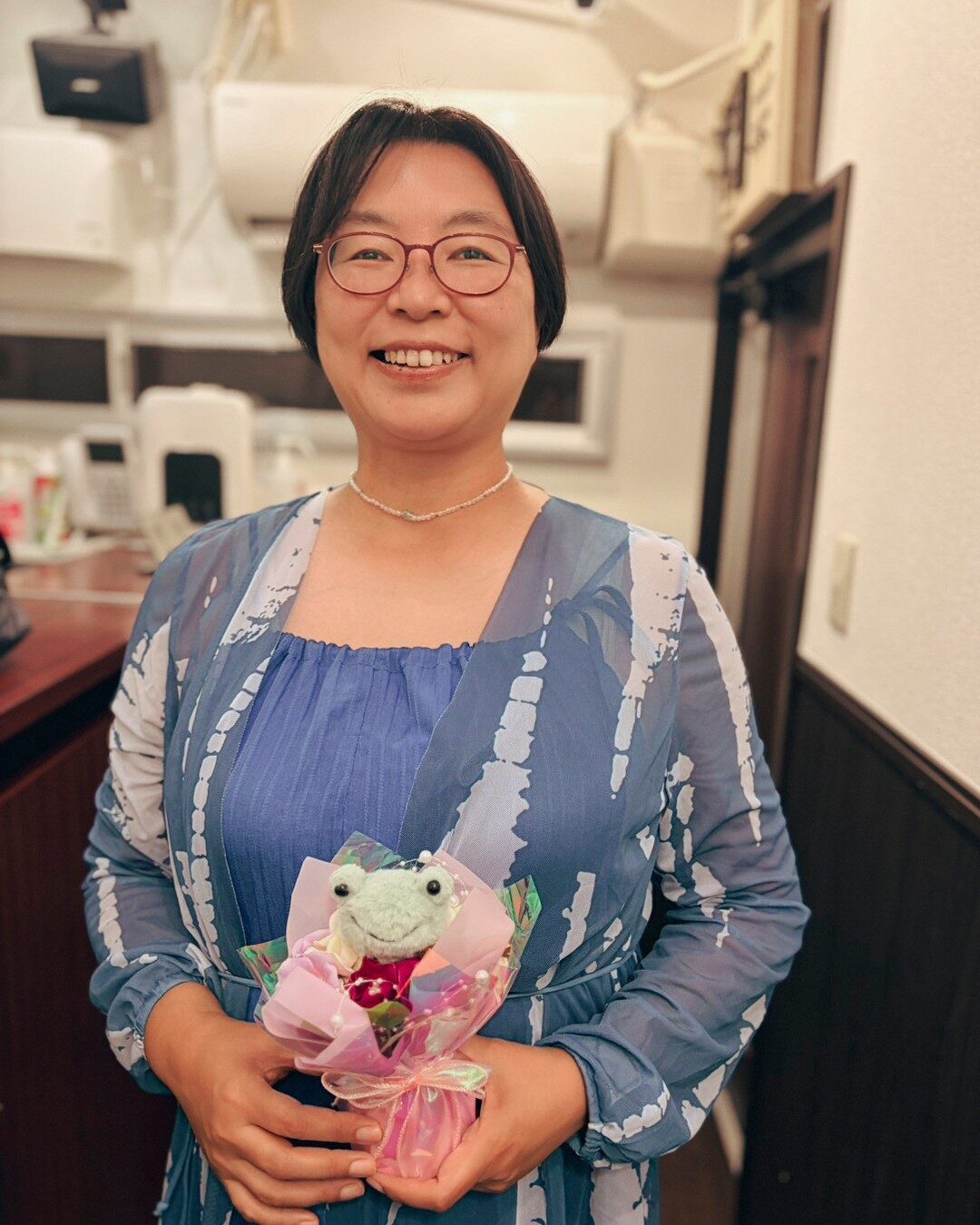 カエルのぬいぐるみが付いた花束を手に、笑顔のPLUM